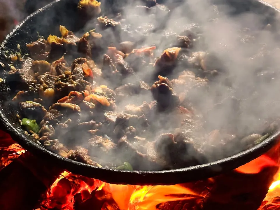 Meat cooking in a pan over a campfire